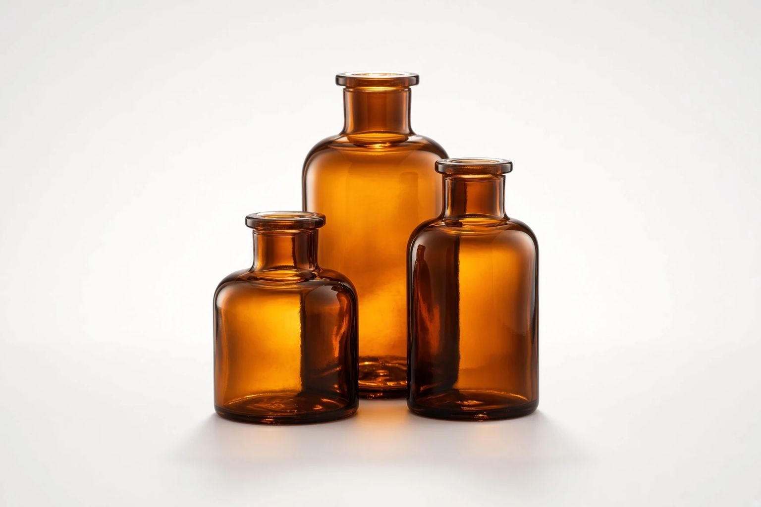 Three amber apothecary bottles of graduating height, backlit on white