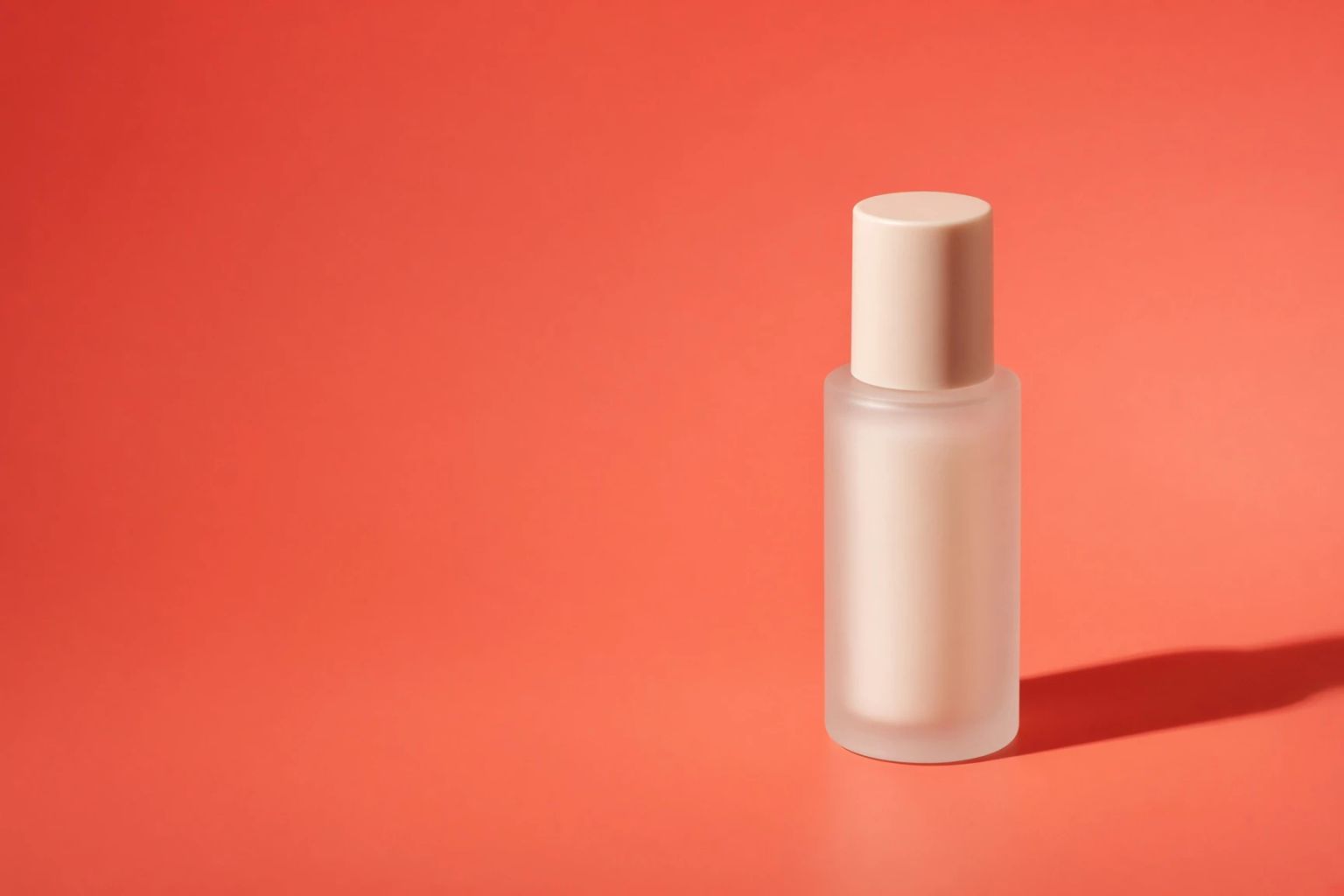 A frosted pink serum bottle casting a hard shadow on a red backdrop